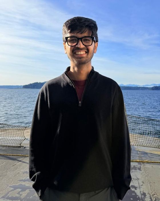 Sarthak Pattnaik smiling on a ferry deck, with water and mountains behind him